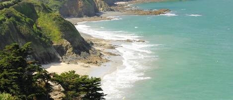 Un paisaje costero con una playa, acantilados y un faro a lo lejos.