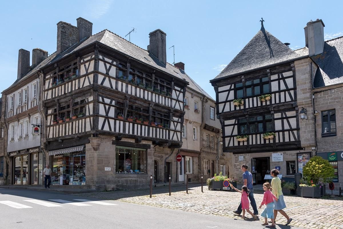 Un edificio tradicional de entramado madera con una calle adoquinada y transeúntes.