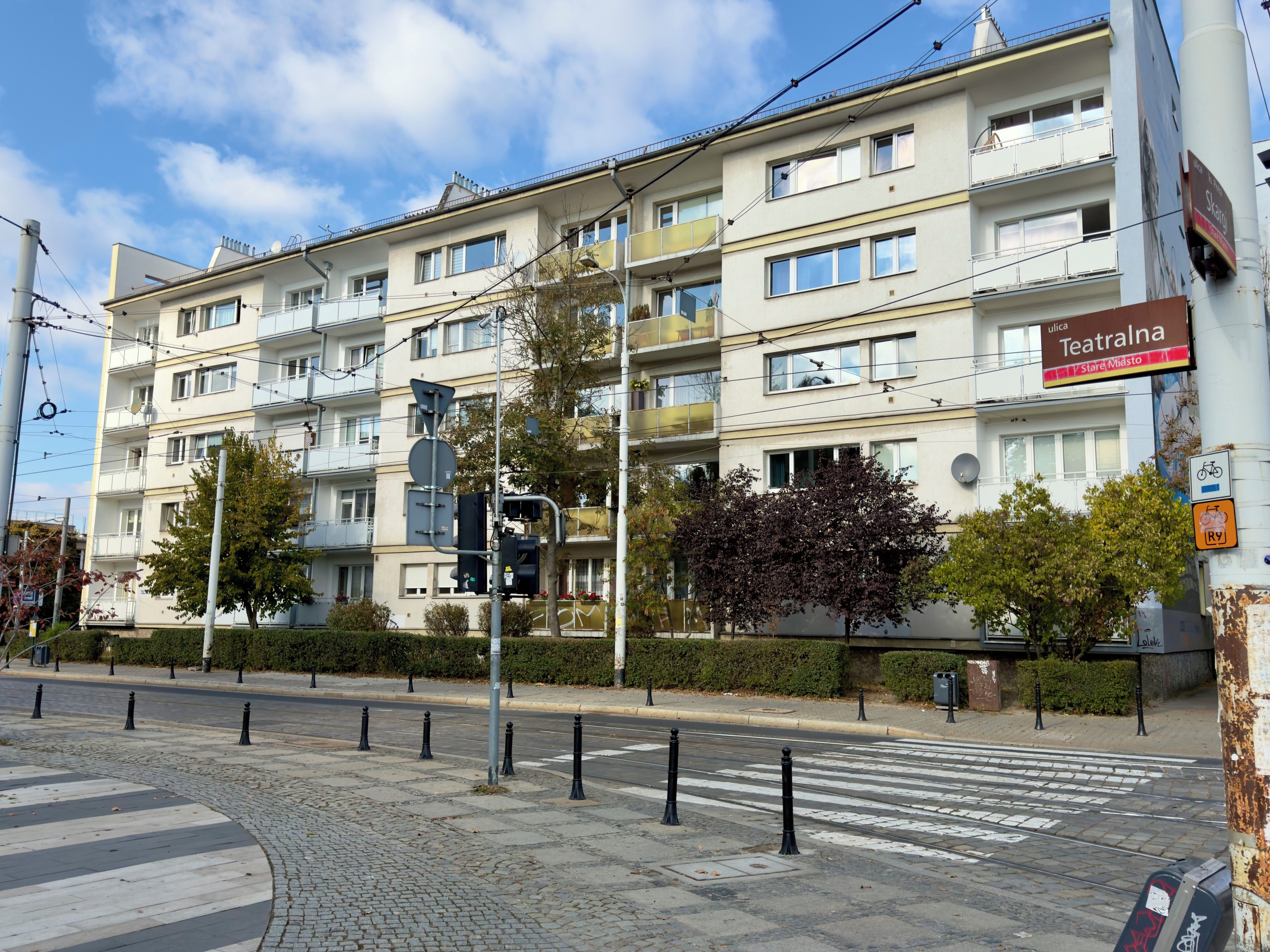 A multi-story building with balconies, a pedestrian crossing, and a tram line.