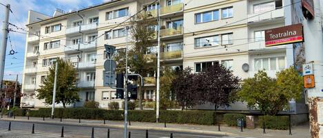 A multi-story building with balconies, a pedestrian crossing, and a tram line.