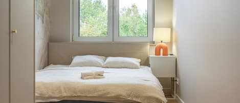 A bedroom with a bed, a nightstand, a lamp, and a window with a view of trees.