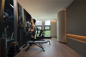 Un gimnasio con equipo de ejercicio, una ventana con vista a edificios y una pared curva.