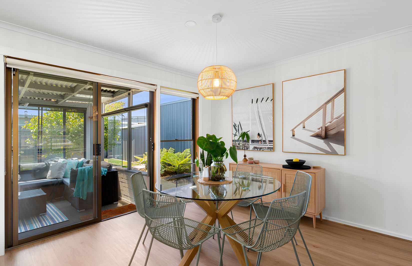 A modern dining area with a glass table, metal chairs, and a hanging light fixture.