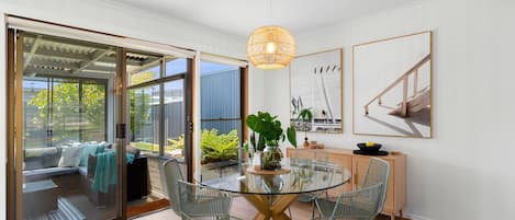A modern dining area with a glass table, metal chairs, and a hanging light fixture.