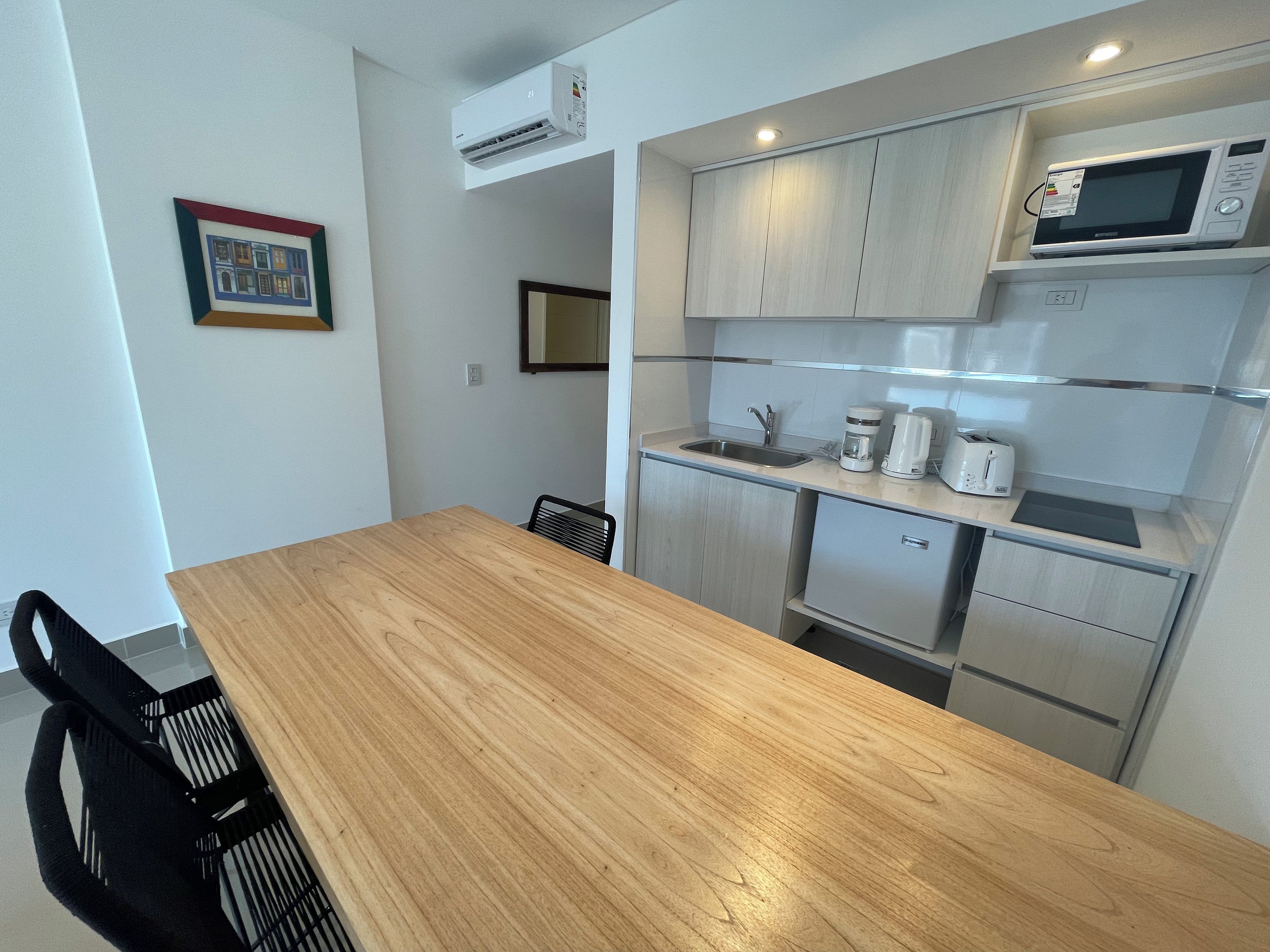 Cocina compacta con mesa de madera, sillas negras, microondas, cafetera y tostadora.