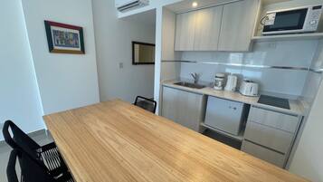 Cocina compacta con mesa de madera, sillas negras, microondas, cafetera y tostadora.