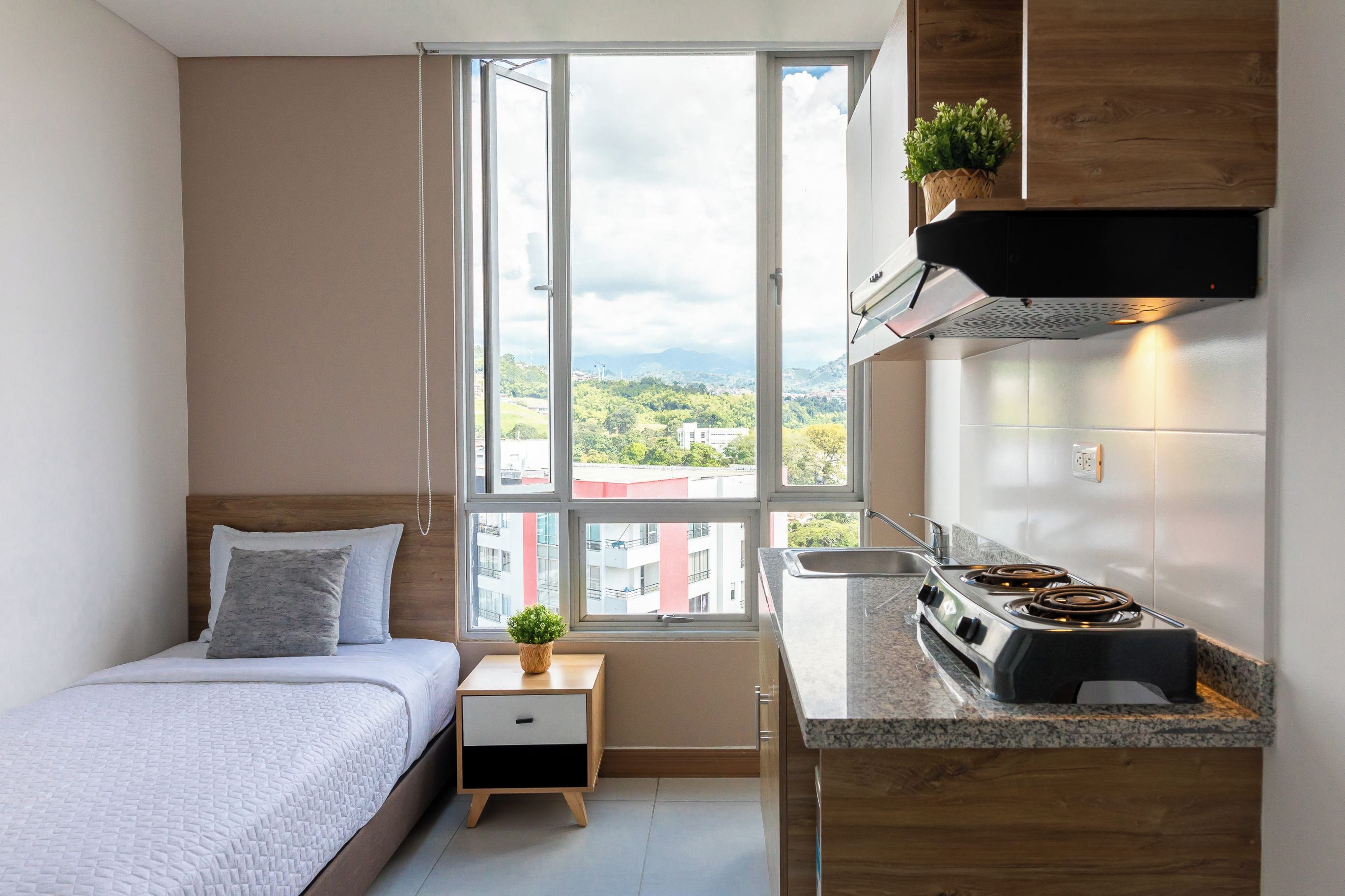 Un dormitorio compacto con cama, mesita de noche y ventana con vista a la ciudad.