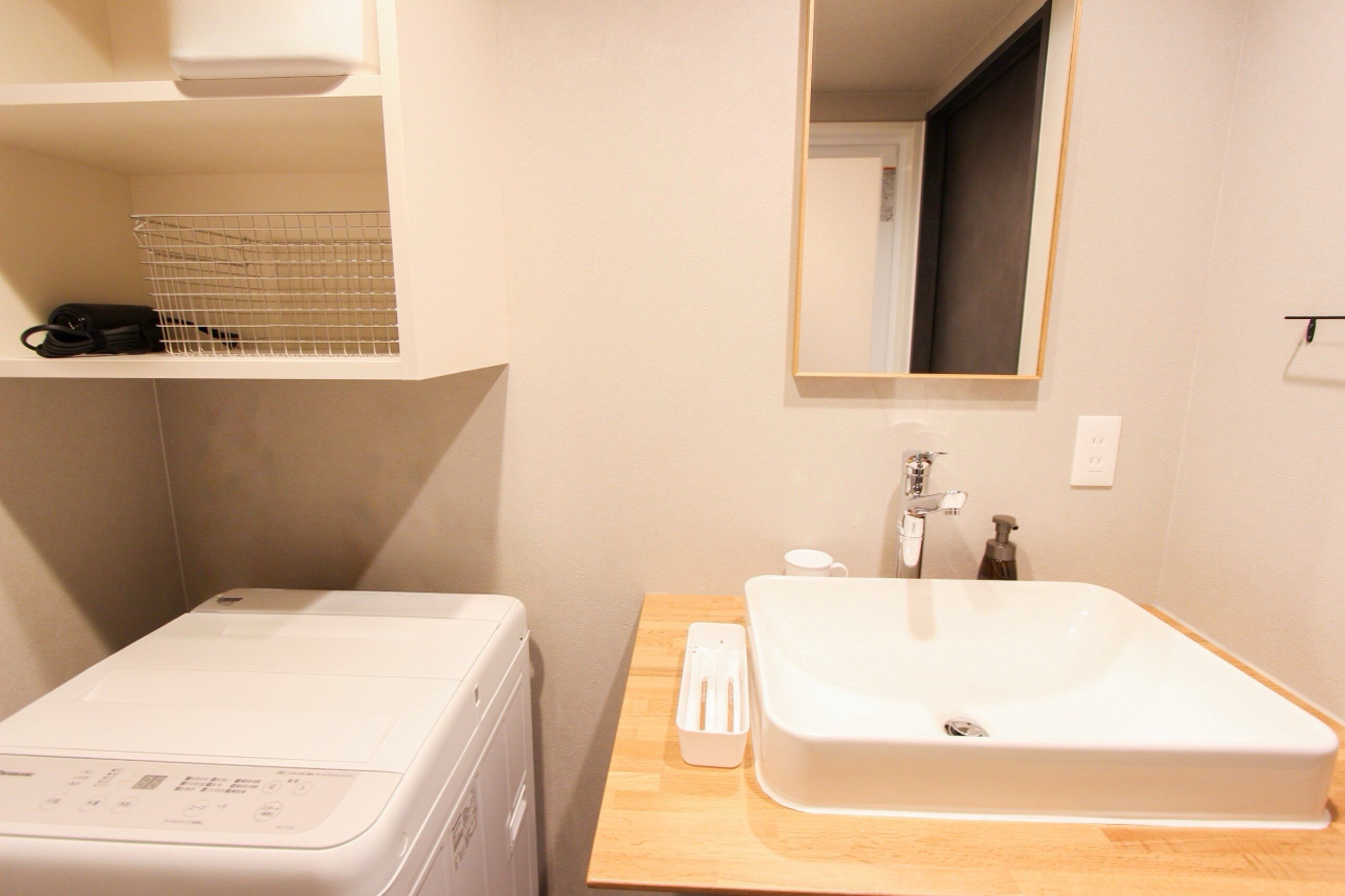 A compact bathroom with a washing machine, a sink, and a mirror.