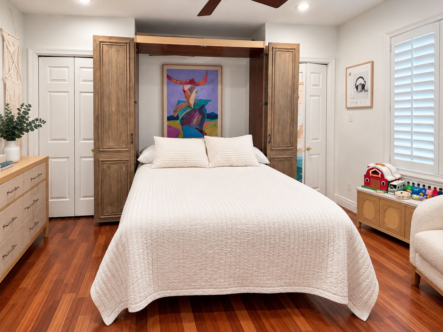 A bedroom with a bed, wooden wardrobe, a painting, a dresser, and a window with blinds.