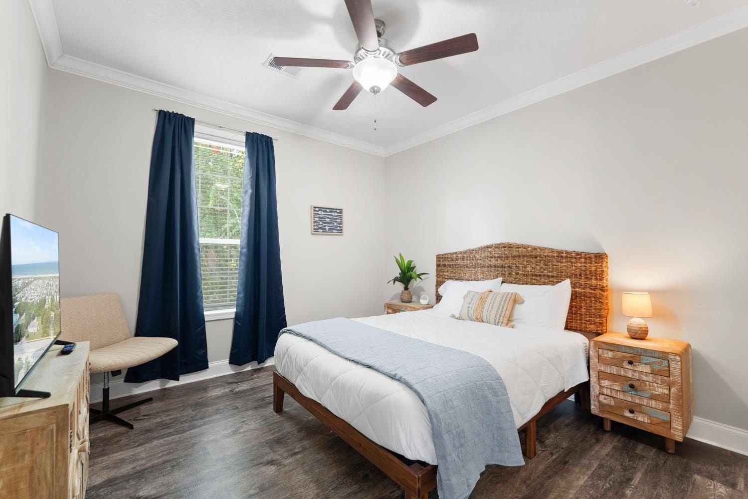 A bedroom with a bed, a desk with a computer, a chair, a nightstand with a lamp, and a ceiling fan.