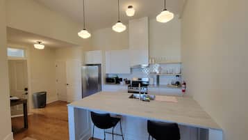 Una cocina moderna con armarios blancos, electrodomésticos de acero inoxidable e iluminación colgante.