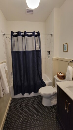 Un baño con cortina de ducha, inodoro, lavabo y suelo de patrón hexagonal.