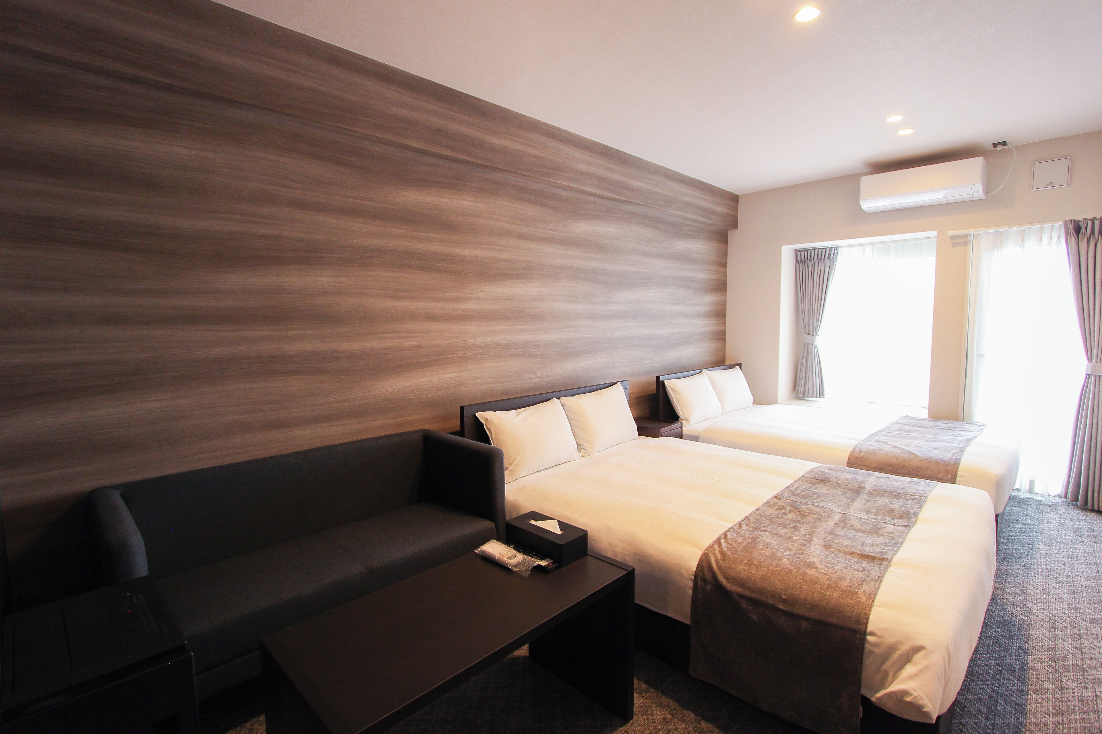 Una habitación de hotel con una cama grande, un sofá, una mesita y una ventana con cortinas.
