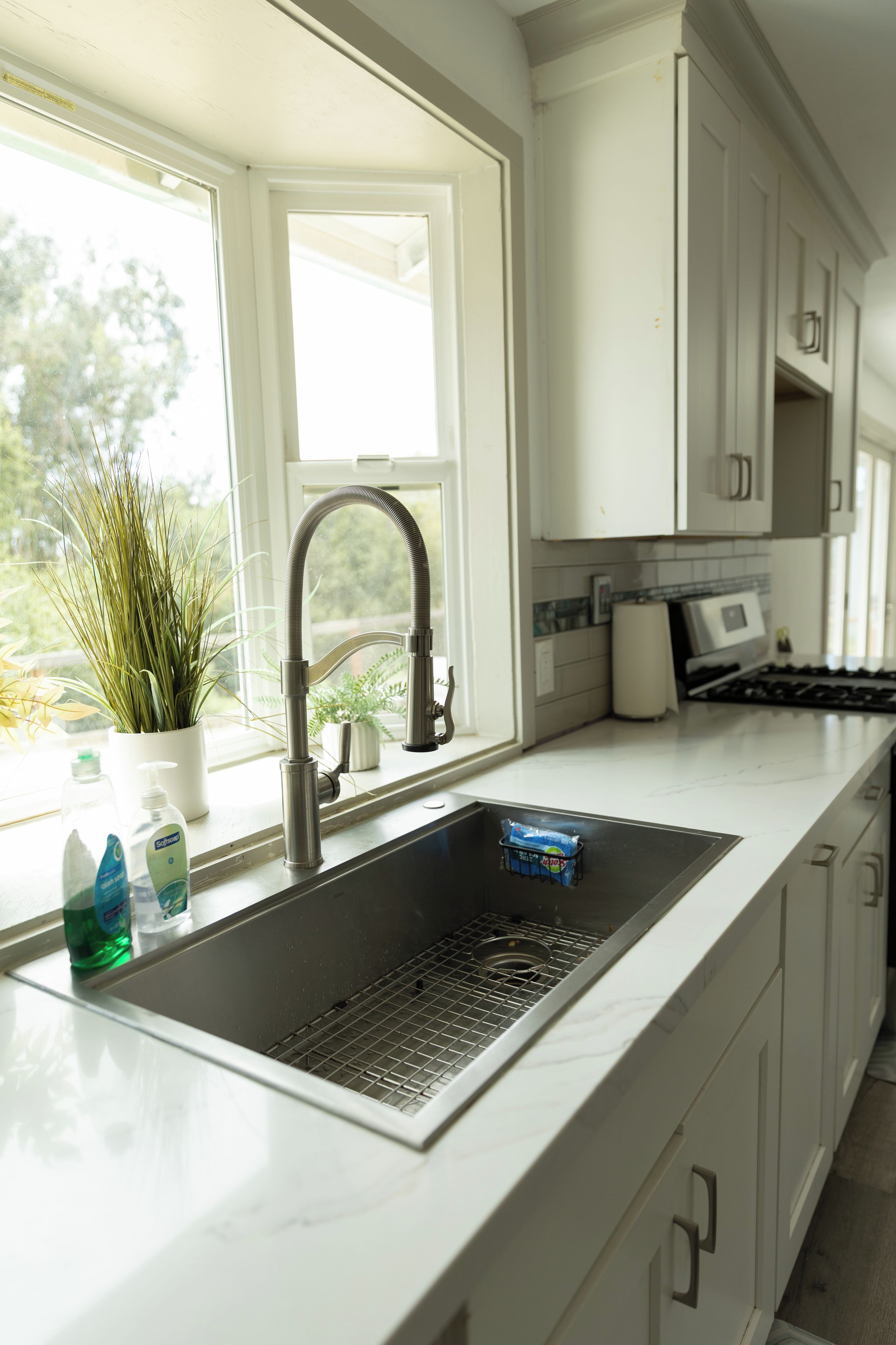 A kitchen with a stainless steel sink, a window, and a potted plant.