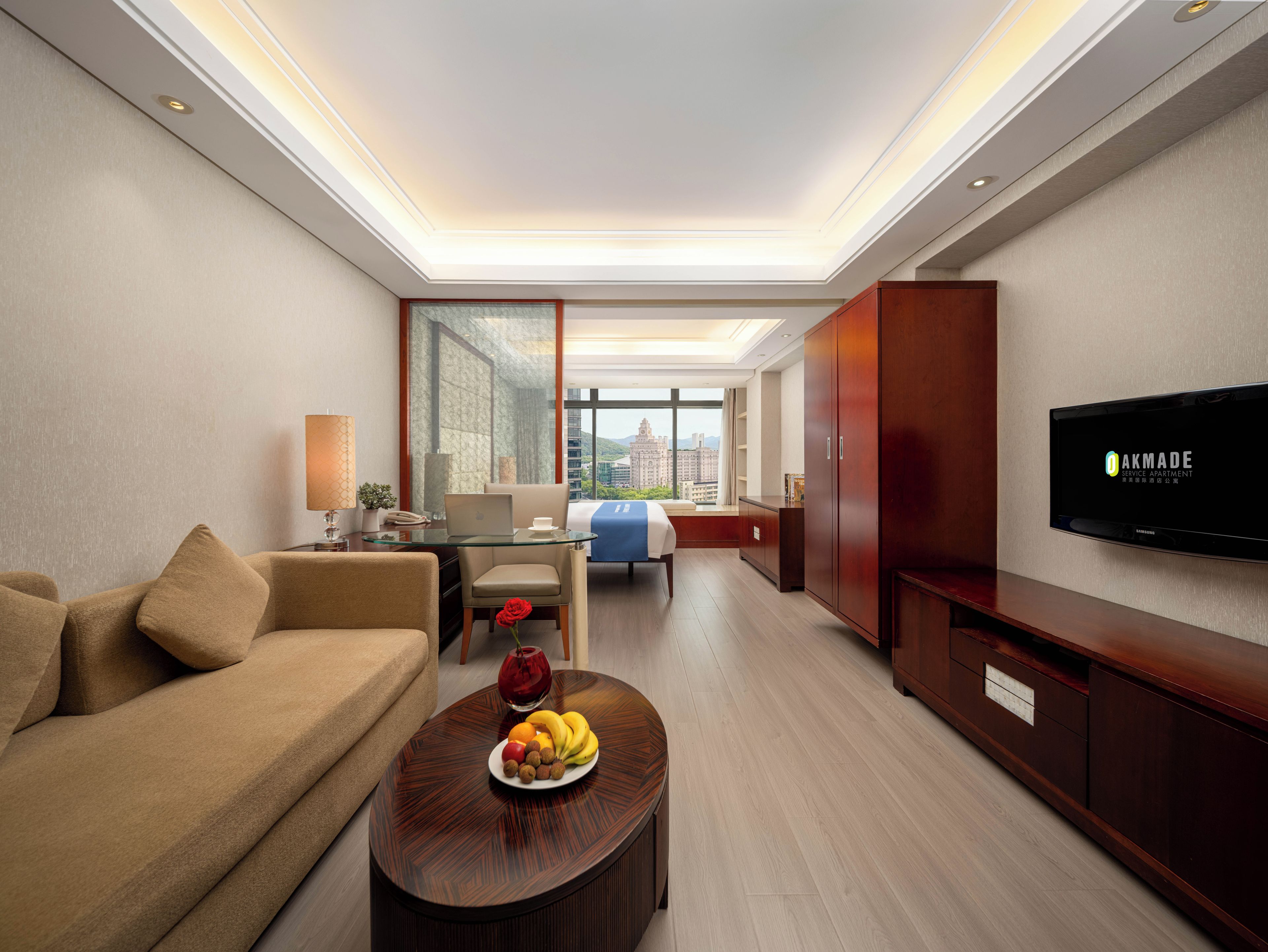 Une chambre d’hôtel moderne avec un canapé, une table à manger avec des fruits, une télévision et une vue sur la ville.