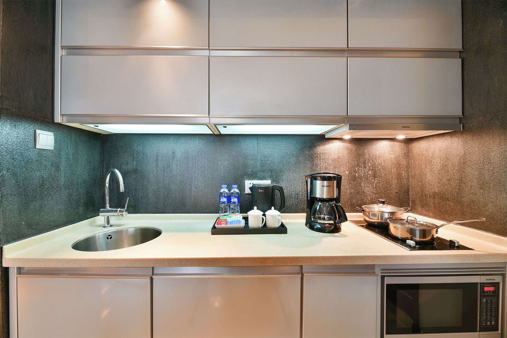 Una cocina moderna con un lavamanos de acero inoxidable, una cafetera Siemens y un microondas.