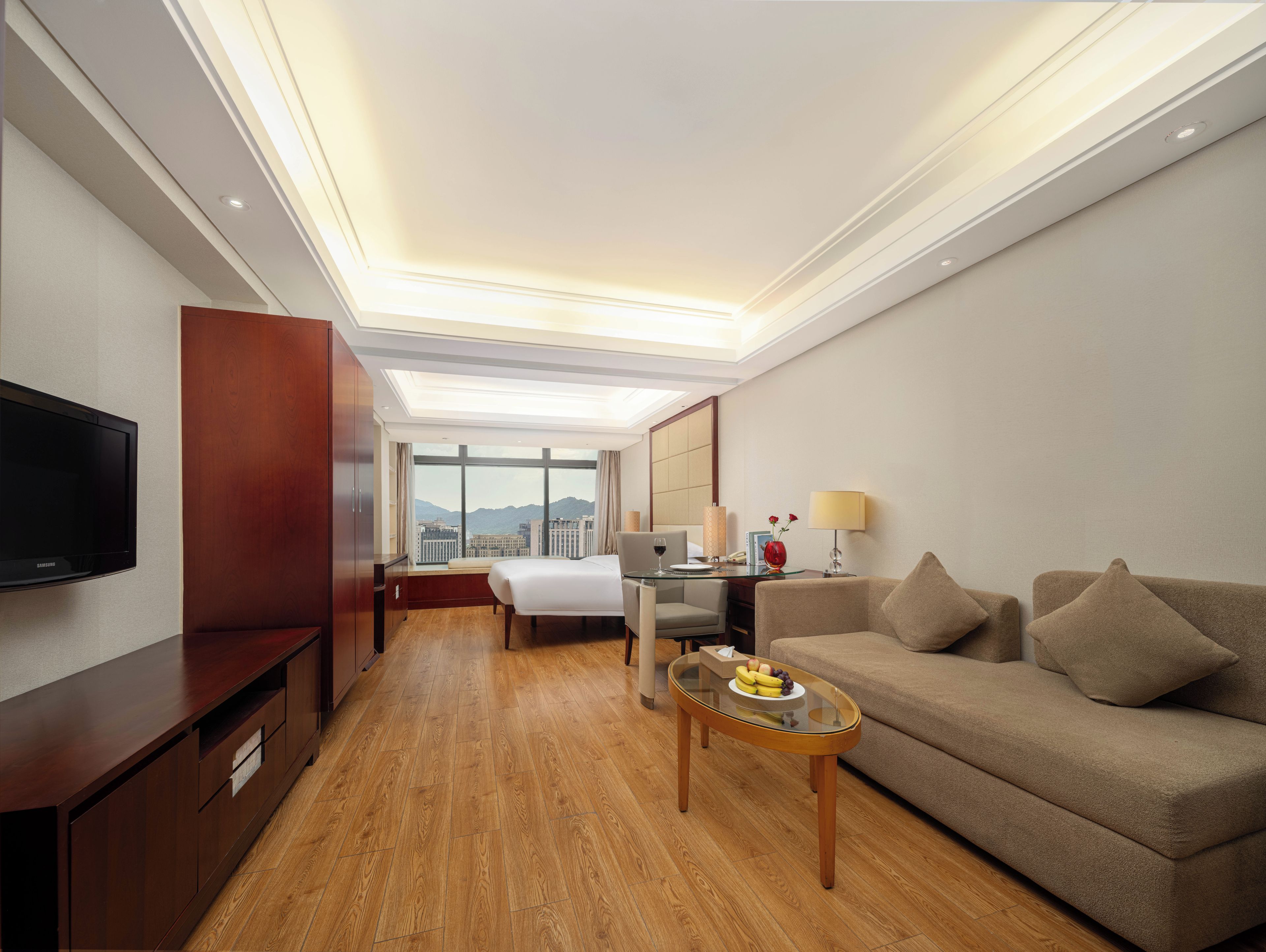 Habitación de hotel con cama, escritorio, televisor, sofá y vistas a la ciudad.