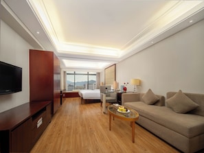 Habitación de hotel con cama, escritorio, televisor, sofá y vistas a la ciudad.