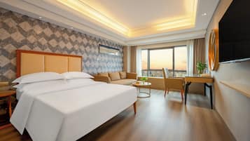 A hotel room with a large bed, a sofa, a desk, and a TV.
