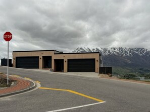 A building with two garage doors, a stop sign, and a mountainous landscape in the background. - Elevated Remarkables Vista | Sweeping Lake Views (Queenstown)