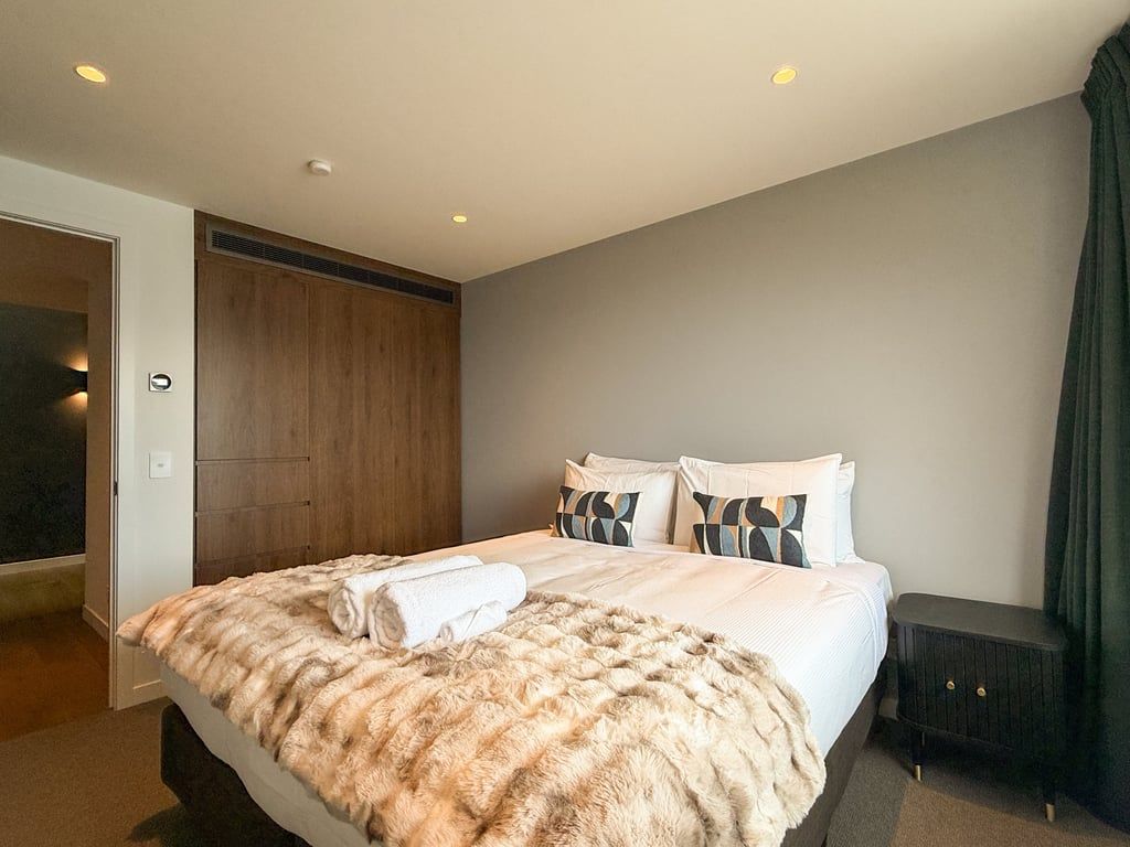 A hotel room with a bed, a nightstand, a wooden wardrobe, and a door leading to another room.