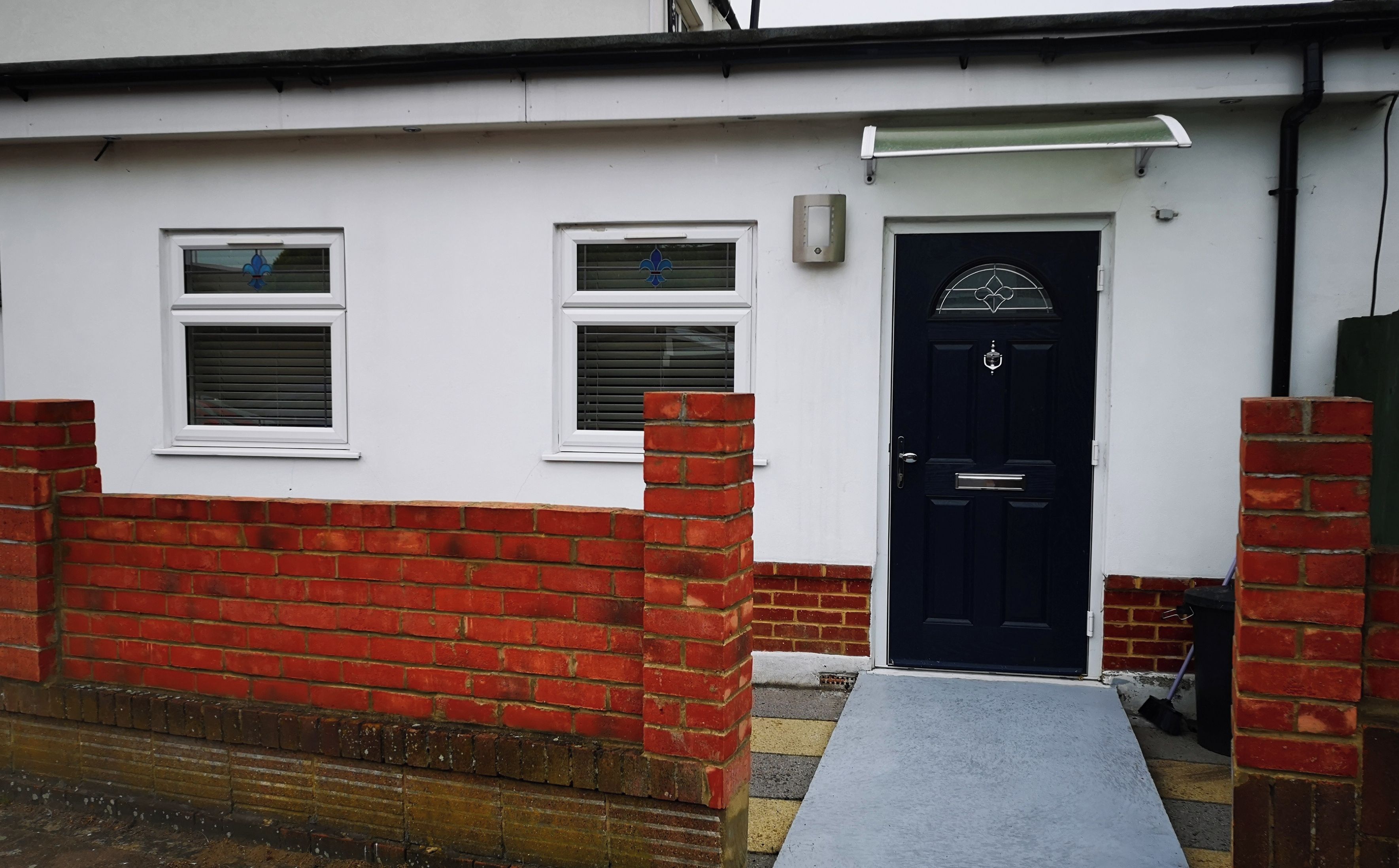 A residential building with a black front door, two windows with shutters, and a red brick wall.
