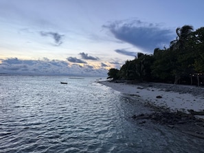 Une plage aux eaux calmes, un petit bateau et une côte rocheuse.