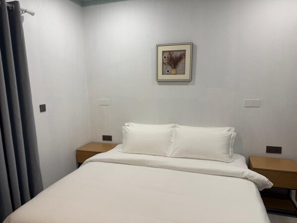 Une chambre d’hôtel avec un lit, deux tables de chevet, un tableau accroché au mur et un rideau.