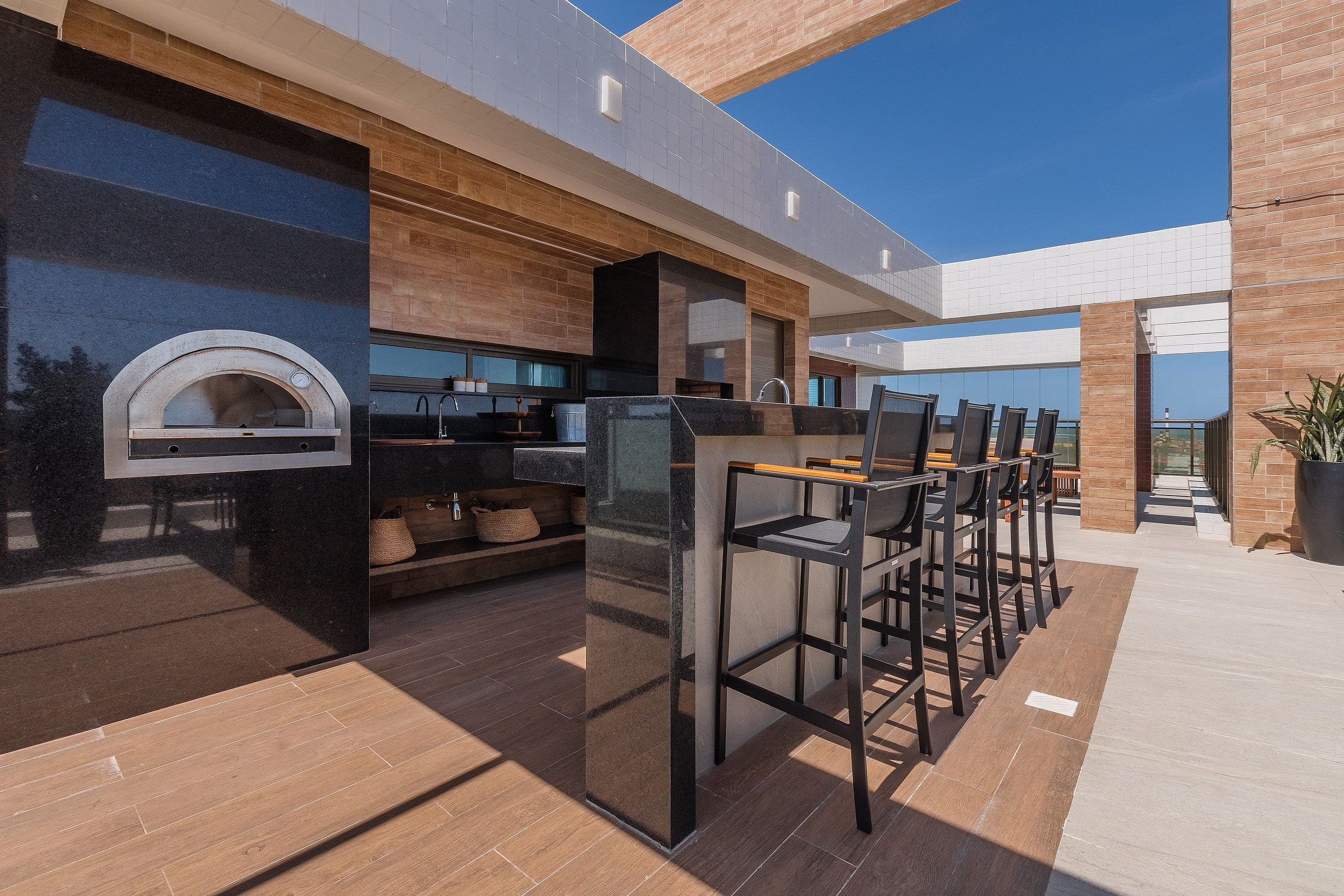 An outdoor kitchen area with a pizza oven, bar stools, and a seating arrangement.