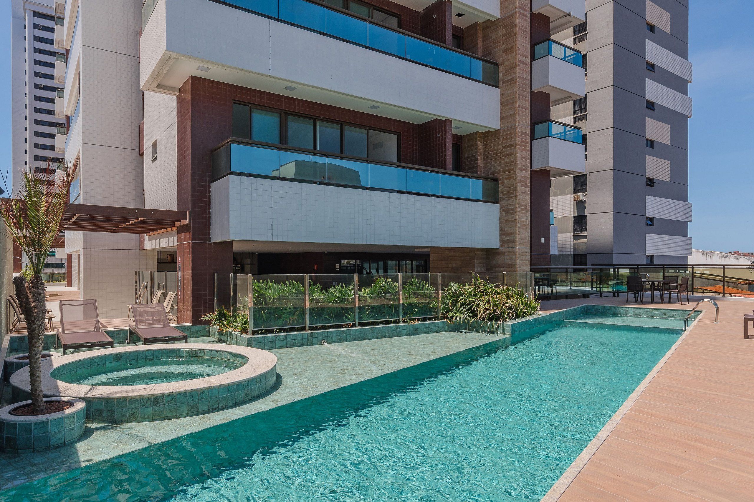 A modern hotel with a swimming pool, outdoor seating, and a view of the surrounding buildings.