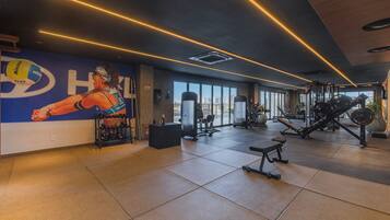 Un gimnasio con equipo de ejercicio, una pared con un jugador de voleibol y vistas a la ciudad a través de amplias ventanas.