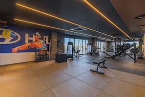 Ein Fitnessstudio mit Trainingsgeräten, einer Wand mit einem Volleyballspieler und Blick auf die Stadt durch große Fenster.