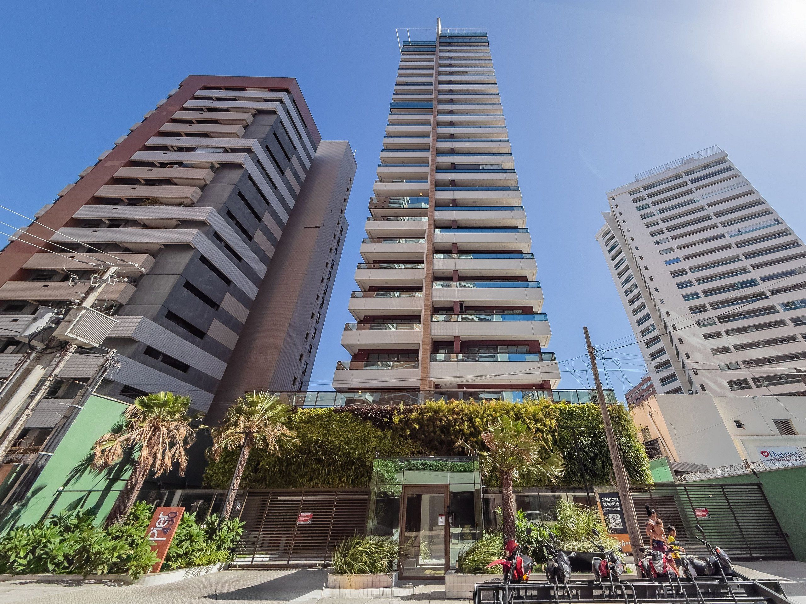 A high-rise building with multiple floors, a gated entrance, and a small garden area with palm trees.