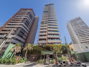 A high-rise building with multiple floors, a gated entrance, and a small garden area with palm trees. - Pier 430 - Near the Beachfront With Pool, Panoramic Rooftop, Gym, Coworking and Complete Leisure Facilities by Carpediem (Fortaleza)