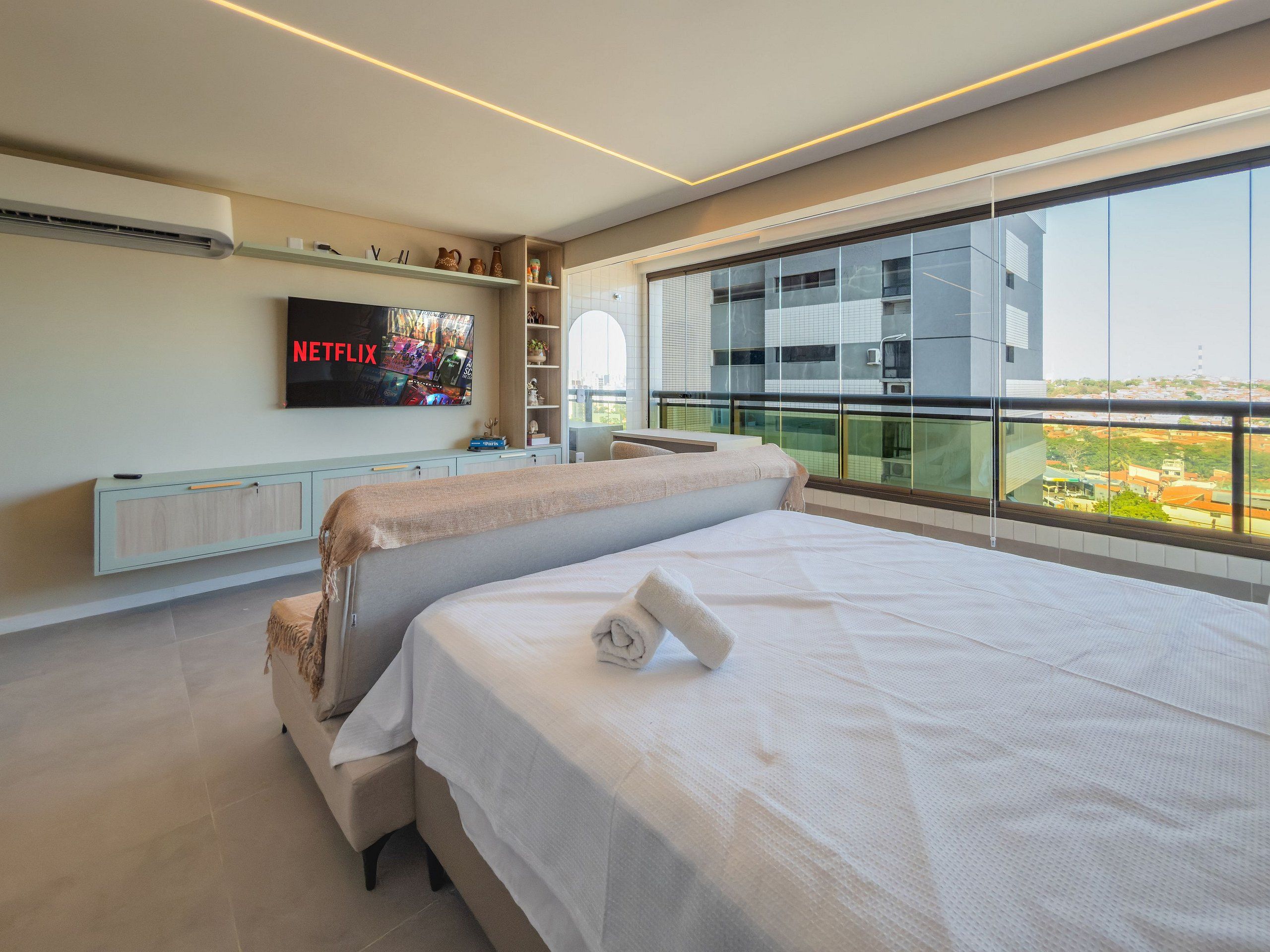 A modern hotel room with a large bed, a TV mounted on the wall, and a balcony with a city view.