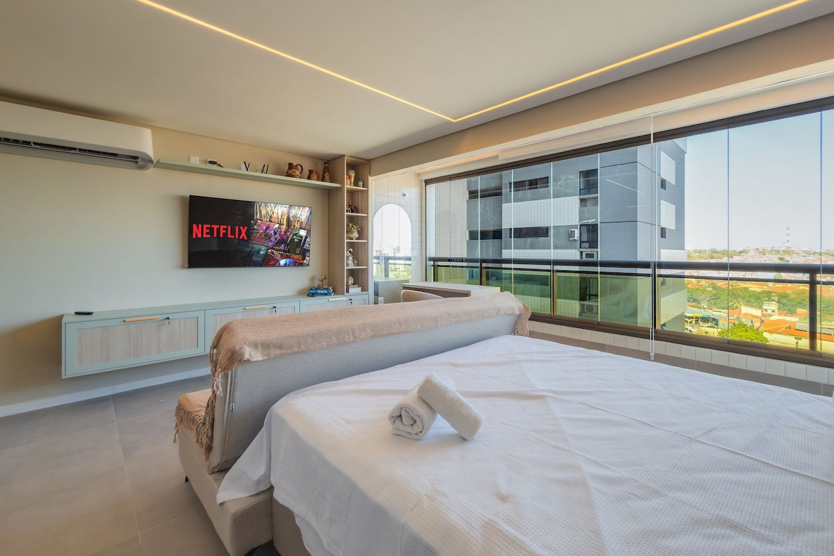 A modern hotel room with a large bed, a TV mounted on the wall, and a balcony with a city view.