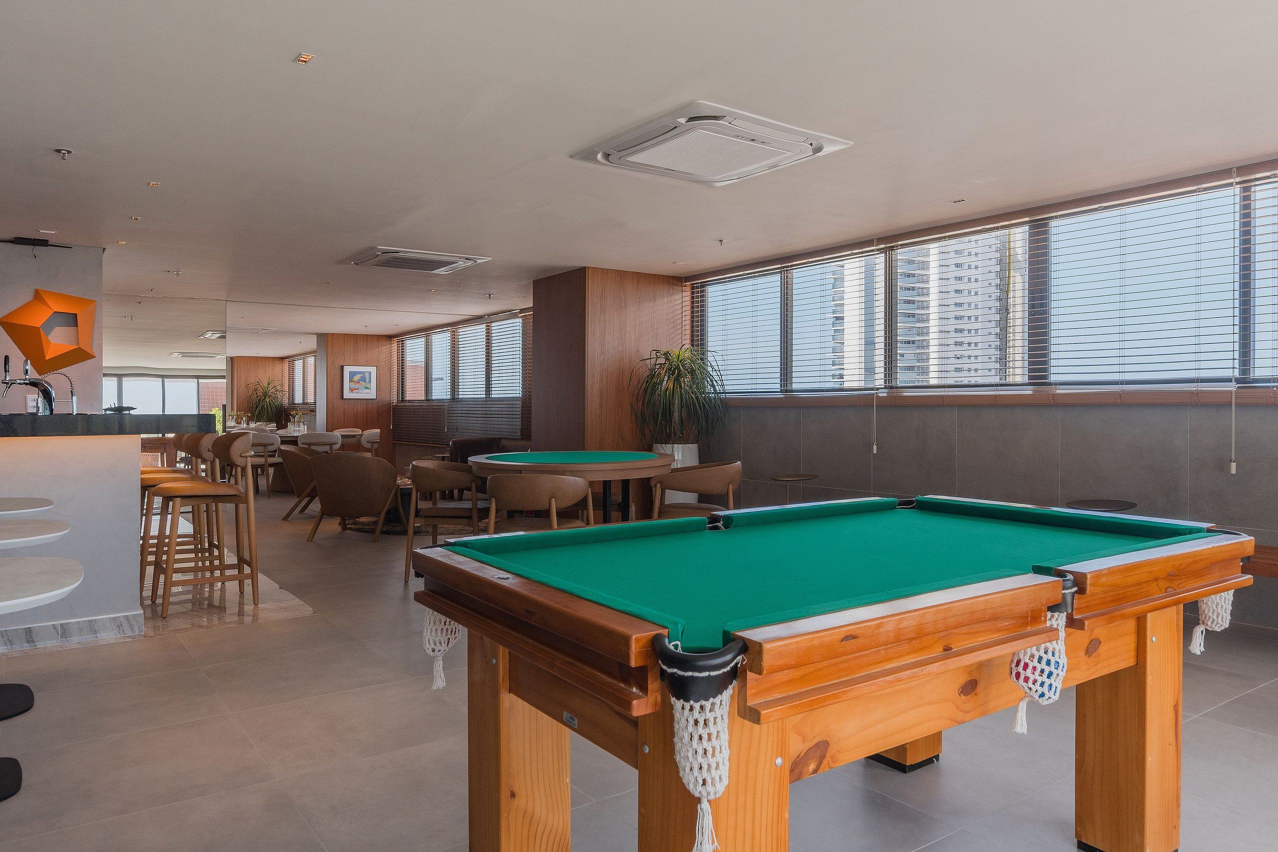 Mesa de billar en una sala con ventanas amplias, una zona de bar y asientos.