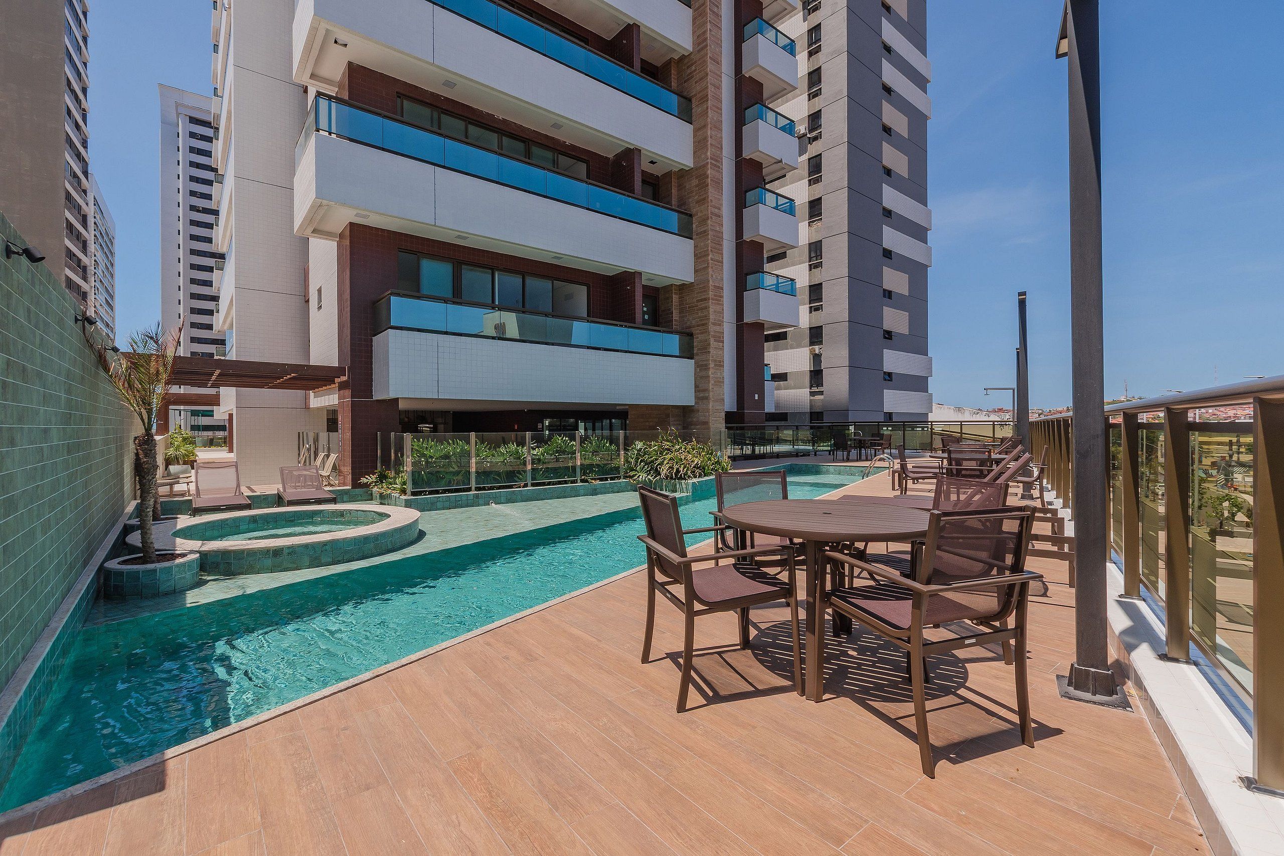A rooftop pool area with a table and chairs, surrounded by a high-rise building with balconies.