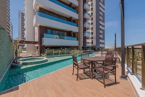 A rooftop pool area with a table and chairs, surrounded by a high-rise building with balconies. - Pier 430 - Near the Beachfront With Pool, Panoramic Rooftop, Gym, Coworking and Complete Leisure Facilities by Carpediem (Fortaleza)