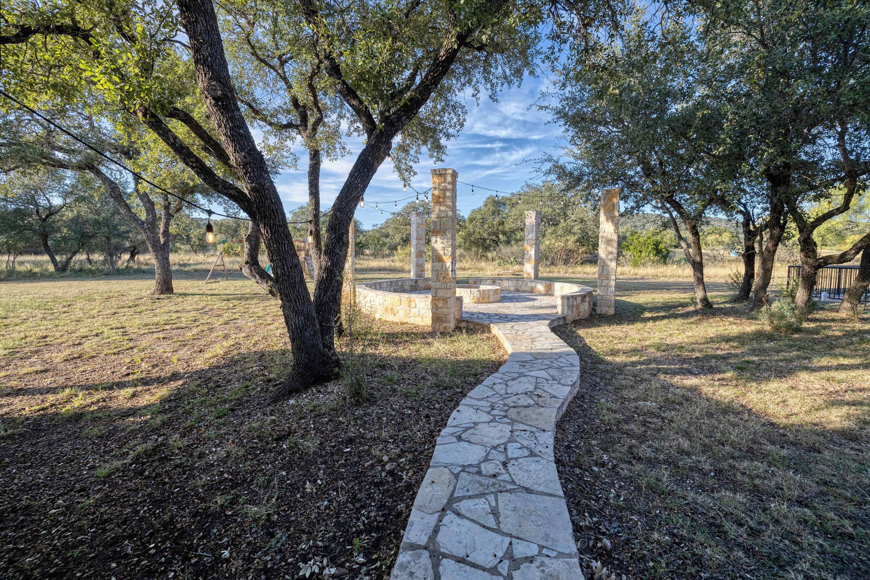 A stone pathway leading to ancient ruins with stone pillars, surrounded by trees and a clear sky.