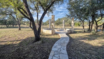 A stone pathway leading to ancient ruins with stone pillars, surrounded by trees and a clear sky.