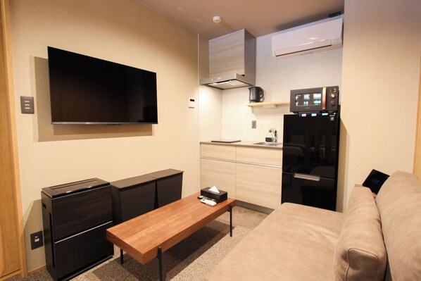 A compact living space with a flat-screen TV, a kitchenette, a sofa, and a coffee table. - Nagasaki Base Sanno (Nagasaki)