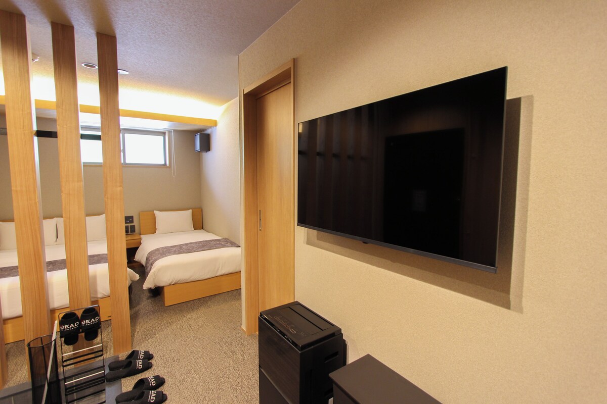 A hotel room with a bed, a television, a desk, and a shoe rack.