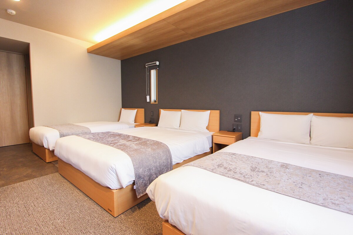 A hotel room with three beds, a dark wall, and a ceiling light.