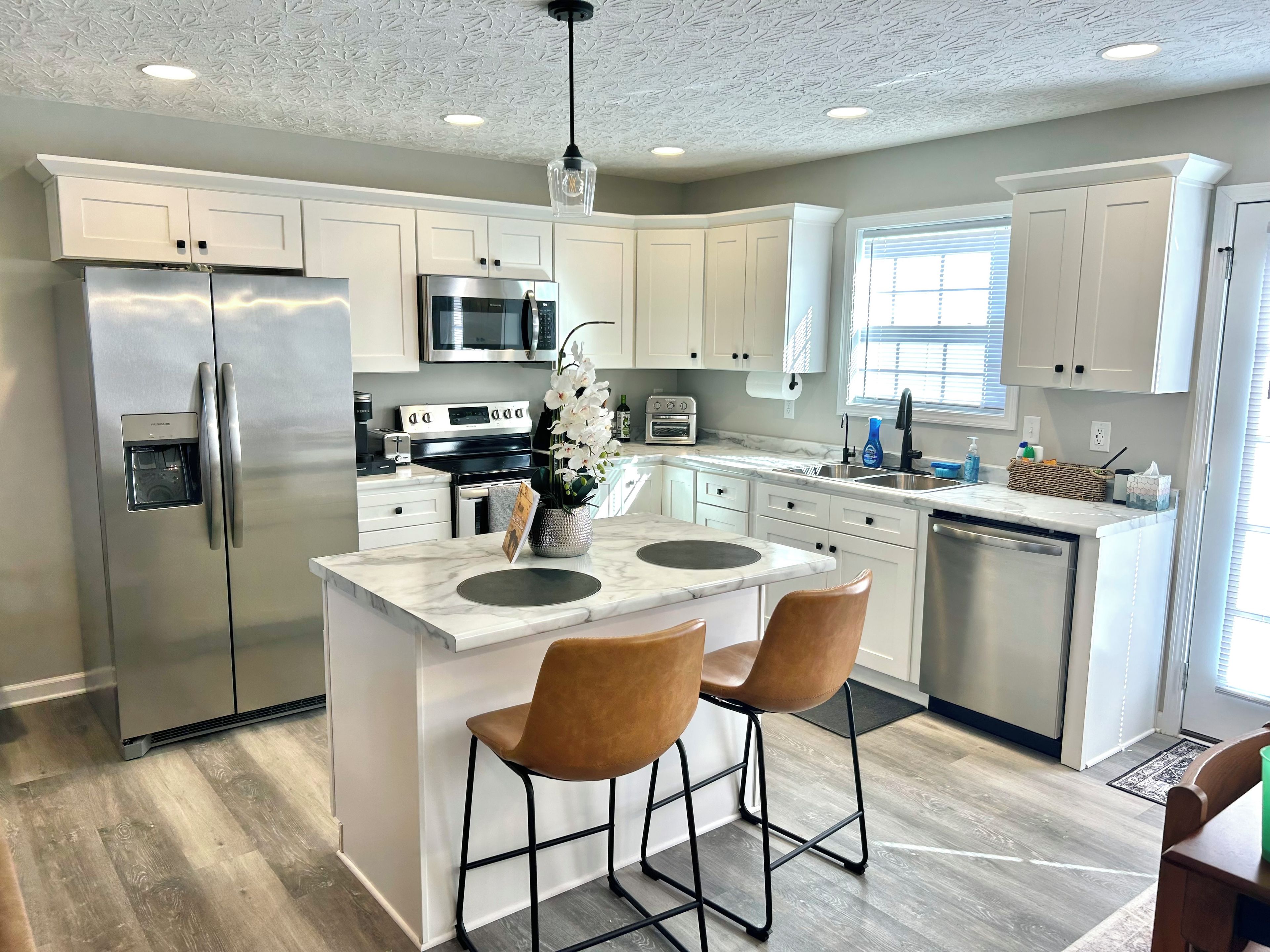 A modern kitchen with white cabinets, stainless steel appliances, and a central island with two bar stools.