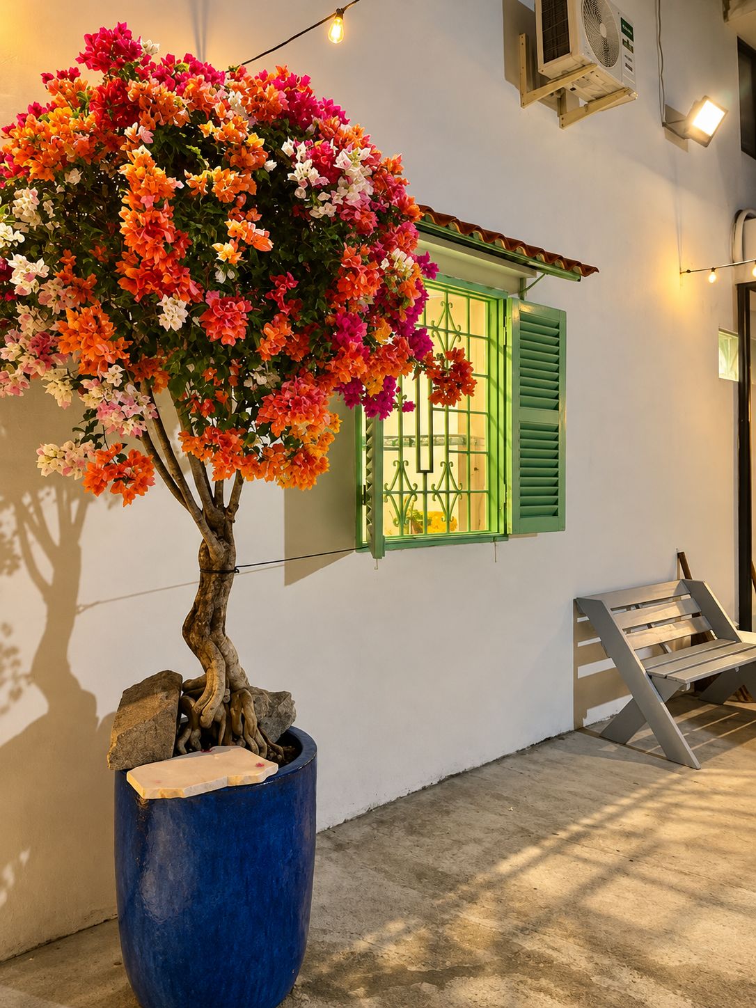 Un árbol en maceta con flores, un banco de metal y una escalera.