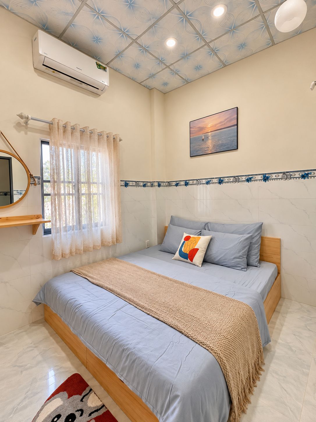 Un dormitorio con cama, ventana con cortinas, aire acondicionado, un cuadro en la pared y techo con diseño geométrico.