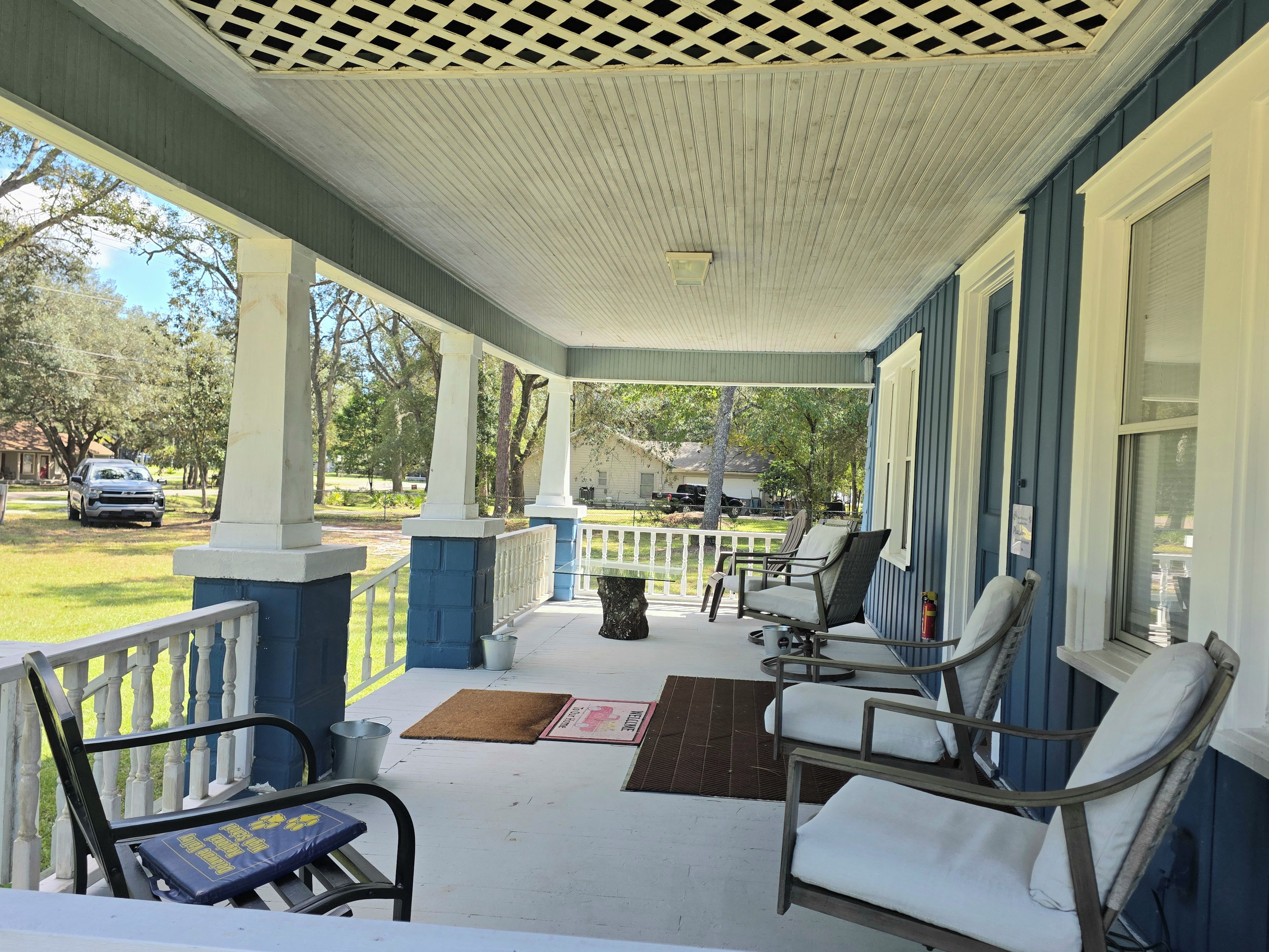 A covered porch with outdoor seating, a view of the yard, and a house in the background.