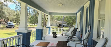 A covered porch with outdoor seating, a view of the yard, and a house in the background.