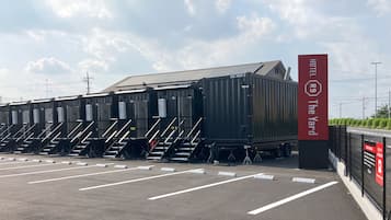 A hotel with a large container-like structure, a parking lot with marked spaces, and a sign indicating the hotel's name.